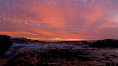 gentle waves crash onto rocky coastline, vivid orange clouds at sunset