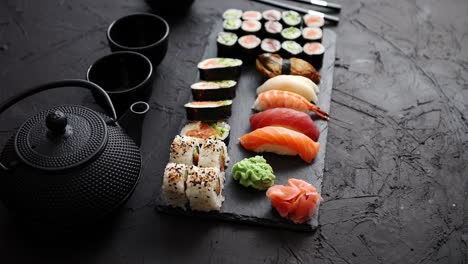 Assortment-of-different-kinds-of-sushi-rolls-placed-on-black-stone-board