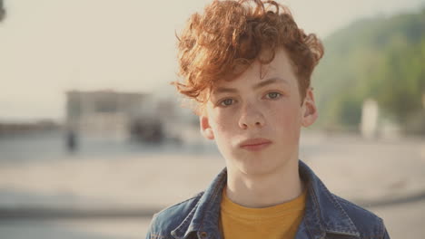 red haired teenager with freckles looks directly into the camera and smiles nervous