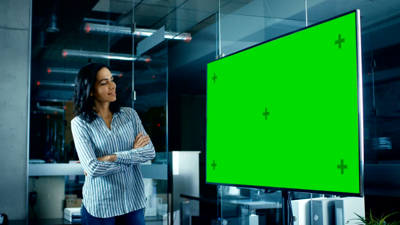 a última hora de la noche, una hermosa mujer hispana mira una maqueta de televisión de pantalla verde en la sala de conferencias.