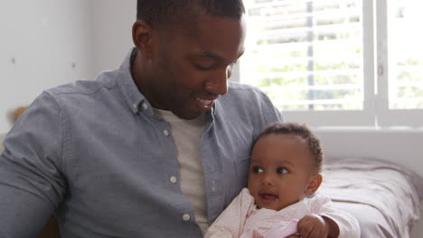 father sitting in nursery chair holding baby daughter