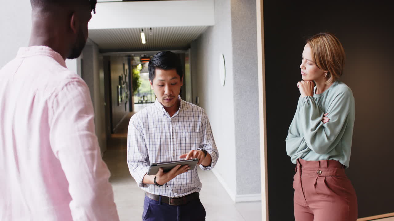 Discussing project details, colleagues using tablet and standing in office hallway