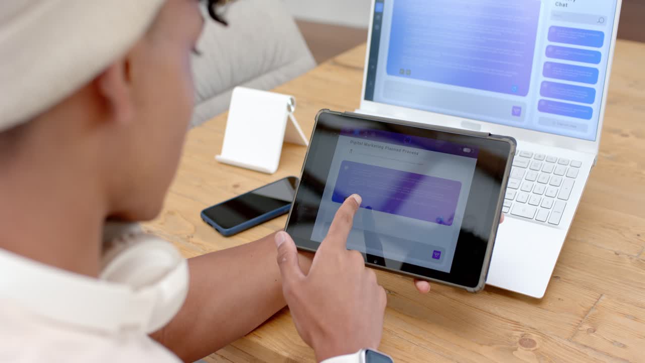 African American man glancing at tablet, tapping purple tile while doing work on laptop, copy space