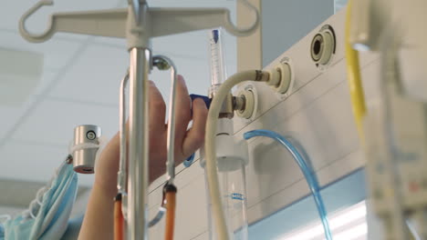 nurse hand adjusts medical flowmeter and humidifier in hospital, close-up