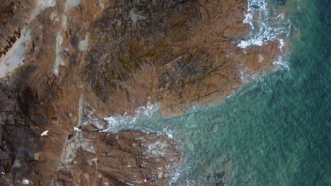 Aerial-top-ascending-view-over-waves-breaking-on-rocky-and-jagged-coast-of-Saint-Malo-in-Brittany,-France