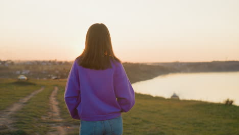 woman walks along riverbank at sunset brunette female tourist enjoys quiet evening at spring