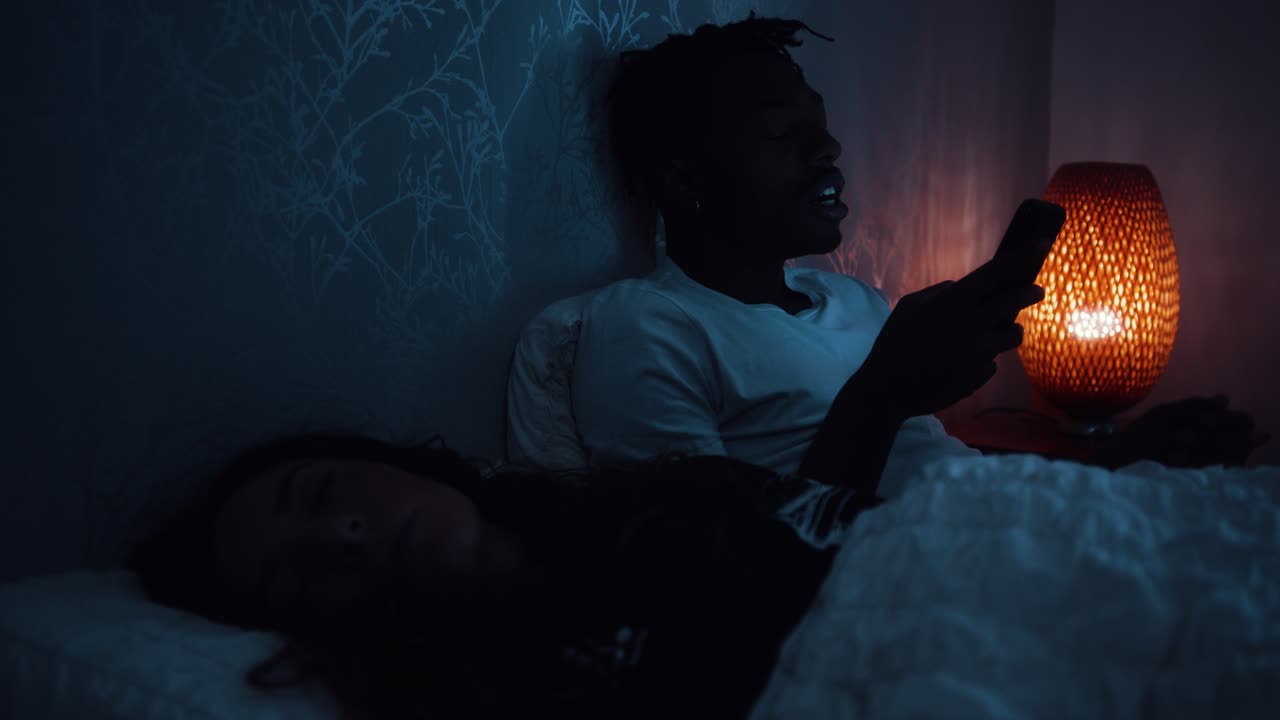 Uomo sbadiglia mentre è seduto a letto a tarda notte sul suo smartphone.