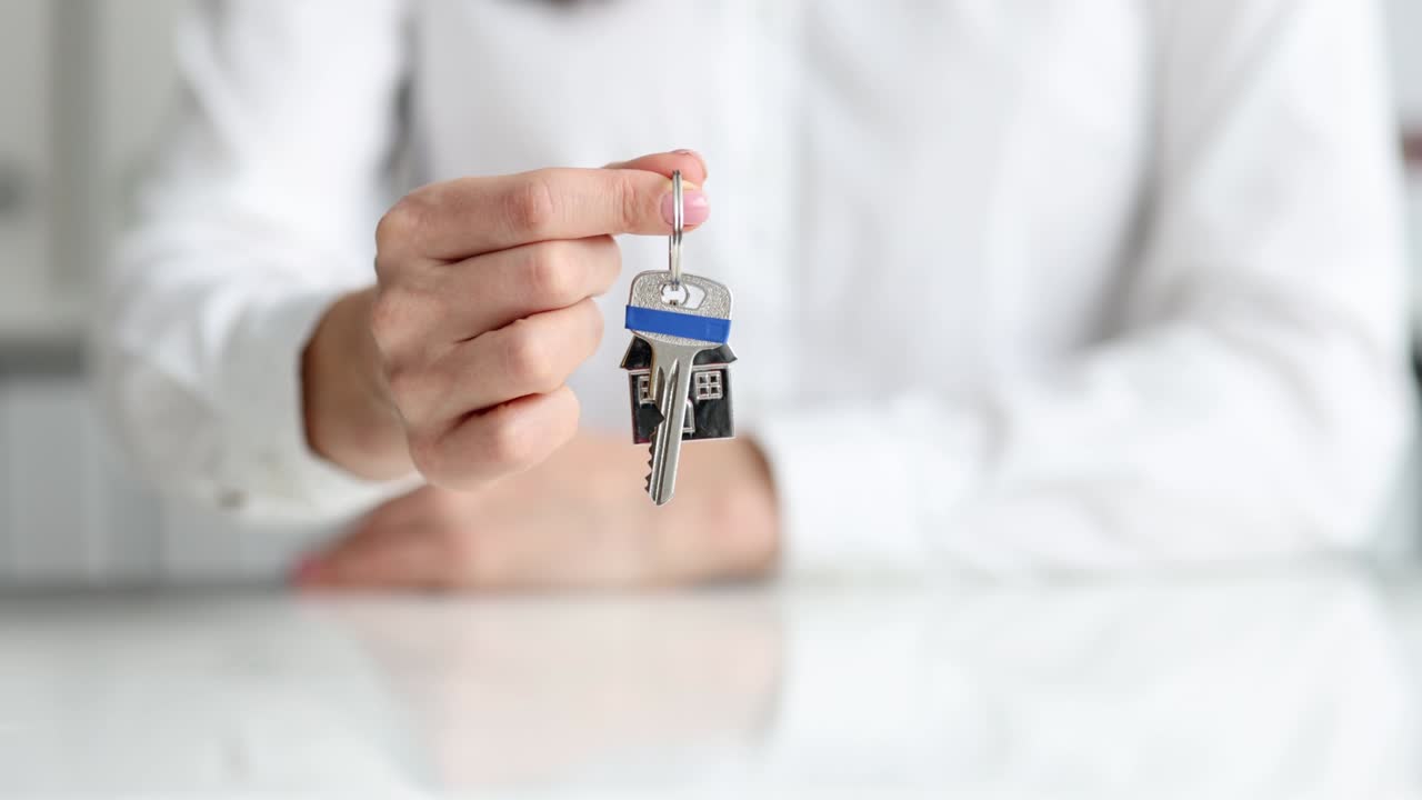 persona sostiene una llave con un llavero de casa pequeña