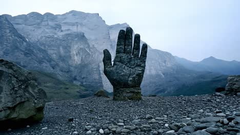 giant stone hand rises from the ground in a rugged mountain landscape, creating a striking symbol of power and mystery