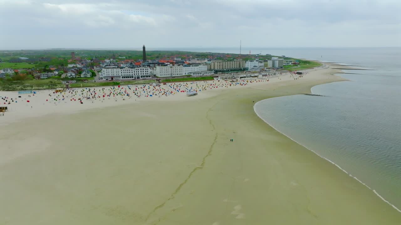 Borkum island resort town with expansive beach and colorful beach baskets. Pan right aerial overlooking beachfront coastline