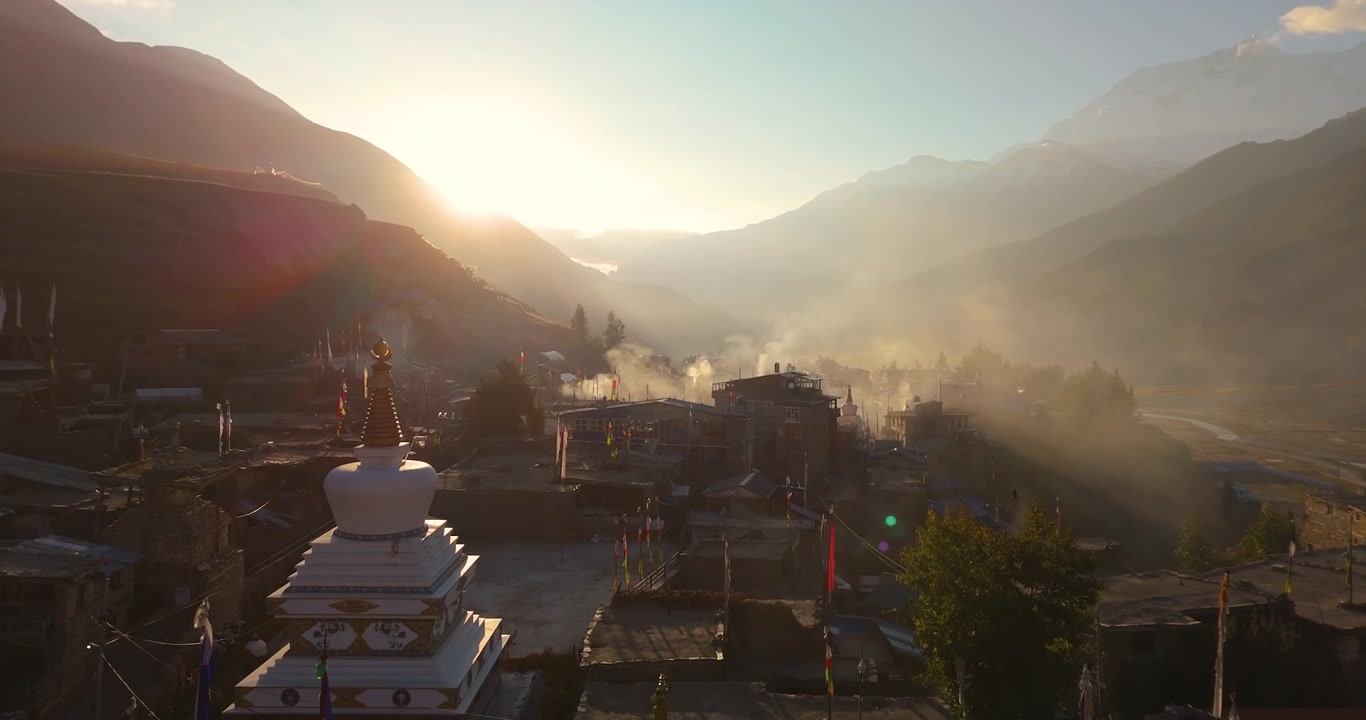 Annapurna Circuit, Manang landsby, Nepal, svævende luftfoto over traditionelle huse med morgenrøgelse, der stiger op under solopgang i Himalaya