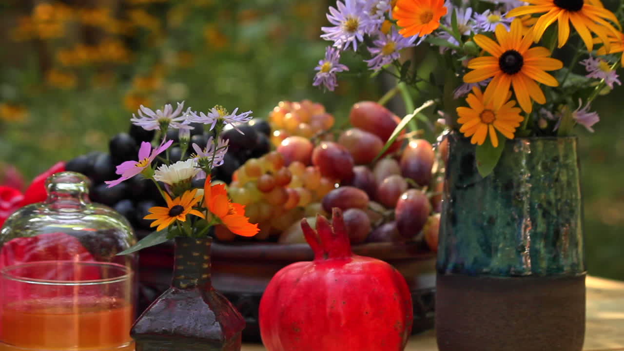 mesa de jardín con cuenco de uvas frescas, granada roja, flores frescas en jarrón en el jardín