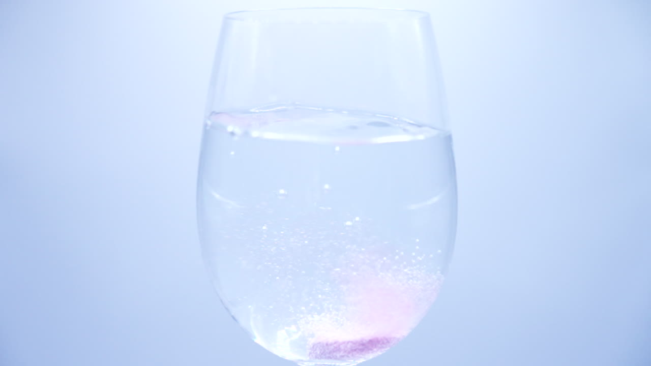 보라색 비타민 정제가 물 한 잔에 떨어지고 용해되어 물이 보라색으로 변하는 느린 동작