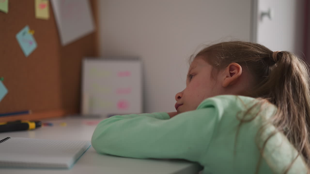 Unhappy little schoolgirl leans on desk while does homework