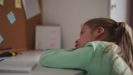 unhappy little schoolgirl leans on desk while does homework