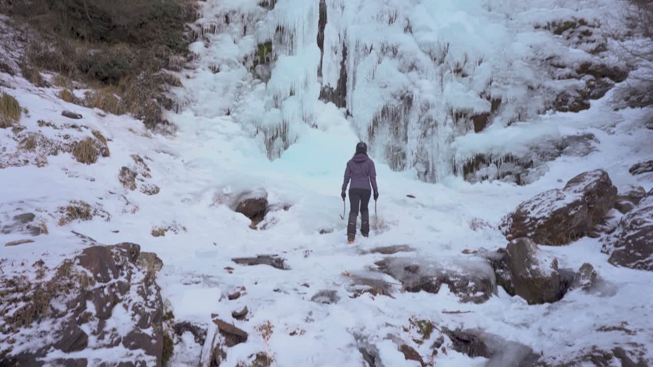 얼음 도끼와 아이젠을 들고 얼어붙은 폭포를 향해 걸어가는 여자