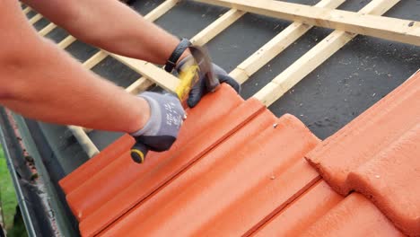 skilled roofer nailing red concrete roof tiles on residential house