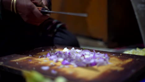 Mujer-De-Piel-Oscura-Cortando-Cebollas-Moradas,-Cuchillo-Grande-De-Brazador-Dorado-Como-Preparación-De-Ingredientes-En-Una-Cocina-Tradicional-Antigua