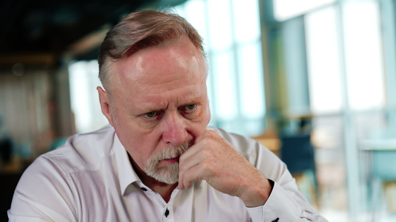 Worried adult Caucasian man takes off his glasses. Man sits holding his hand at the cheek thinking over something. Close up.
