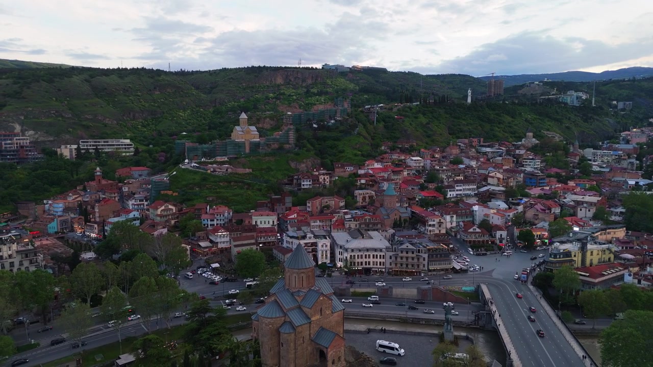 Pemandangan udara Kota Tua Tbilisi, menampilkan rumah-rumah bersejarah dengan balkon berukir, Biara Tabor di bukit, dan lalu lintas perkotaan di kaki punggung bukit benteng Narikala di Georgia.