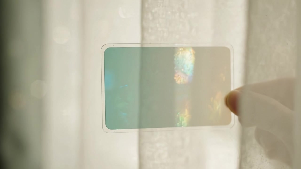 Una mano sostiene una tarjeta translúcida contra un fondo suavemente iluminado, parcialmente oculta por delicadas cortinas, creando un intrigante juego de luces y sombras.