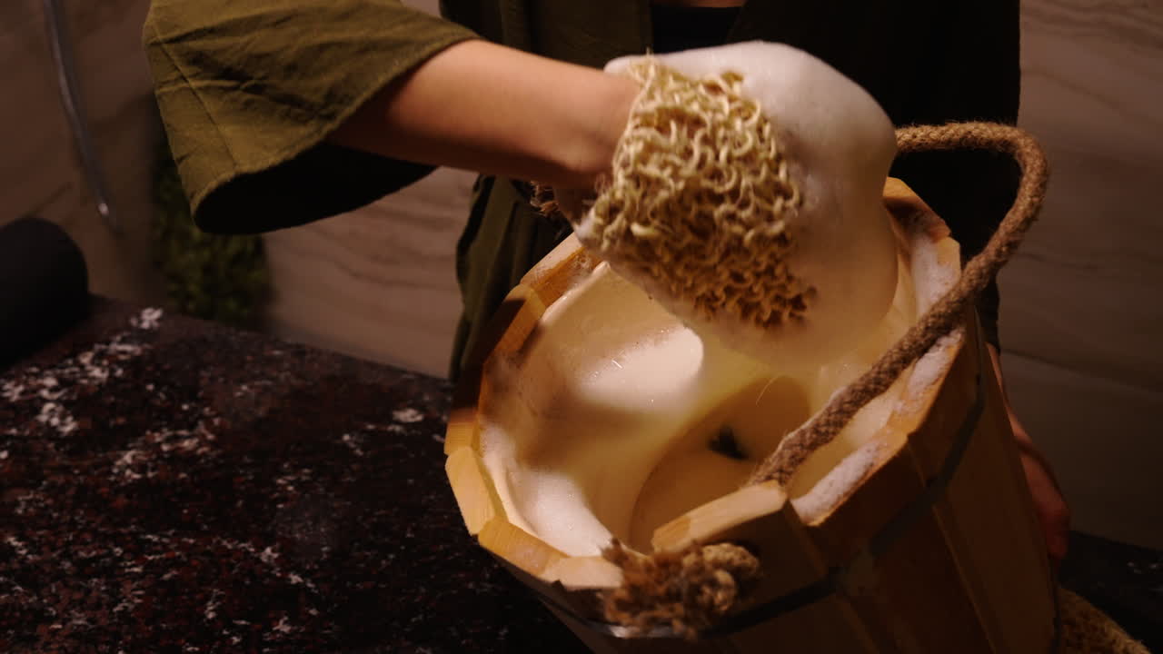 Woman using a wooden bucket and loofah for a bath or spa treatment