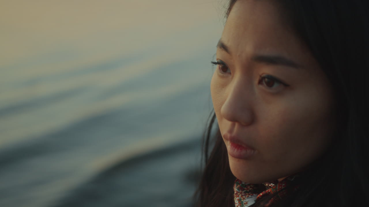 해가 지는 동안 차분한 물 위를 쳐다보는 사려 깊은 여자