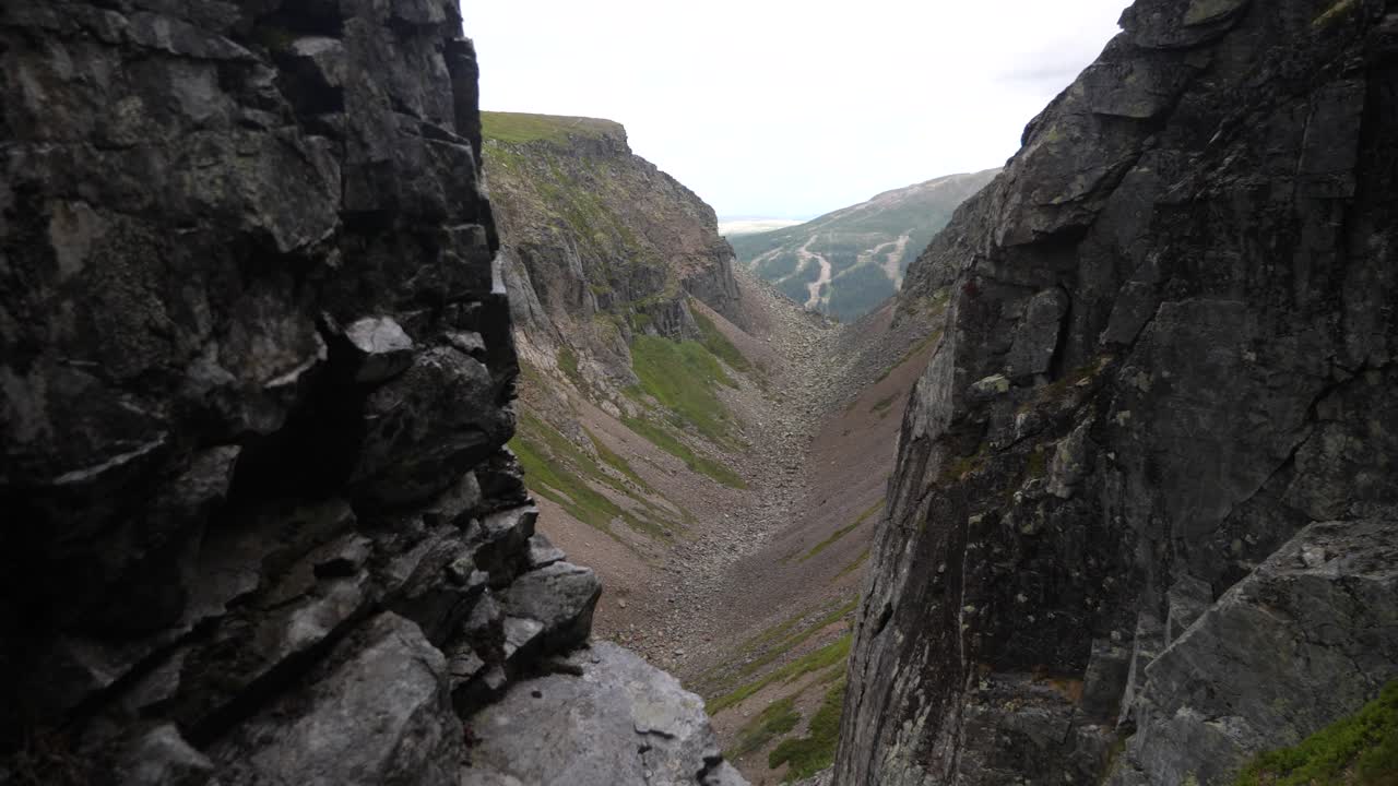 disparo revelador de diapositivas que acecha detrás de una pared rocosa, revelando un gran valle verde en la reserva natural de bastudalen, jämtland, suecia