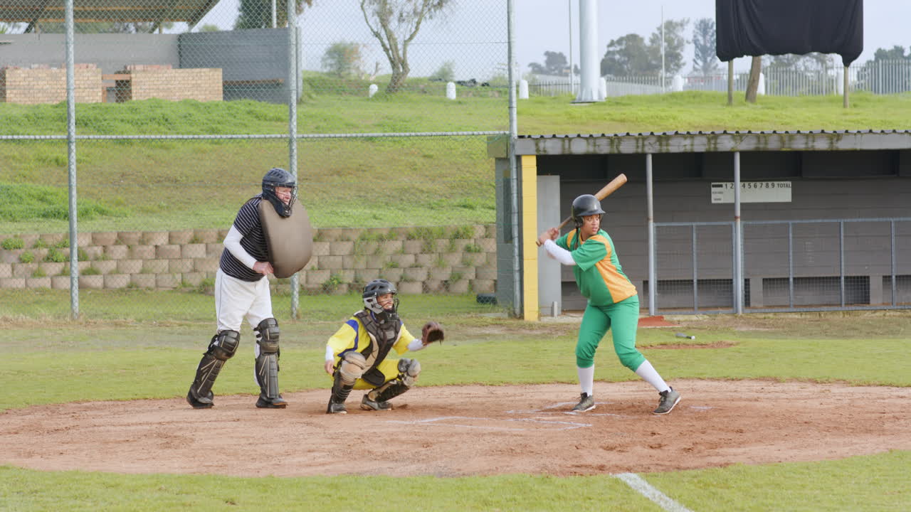 Giocatrici di baseball multietniche e arbitro uomo che battono la palla e corrono su un campo da gioco.