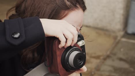 Young-Caucasian-brunette-woman-taking-photograph-outside-with-camera,-close-up-slow-motion