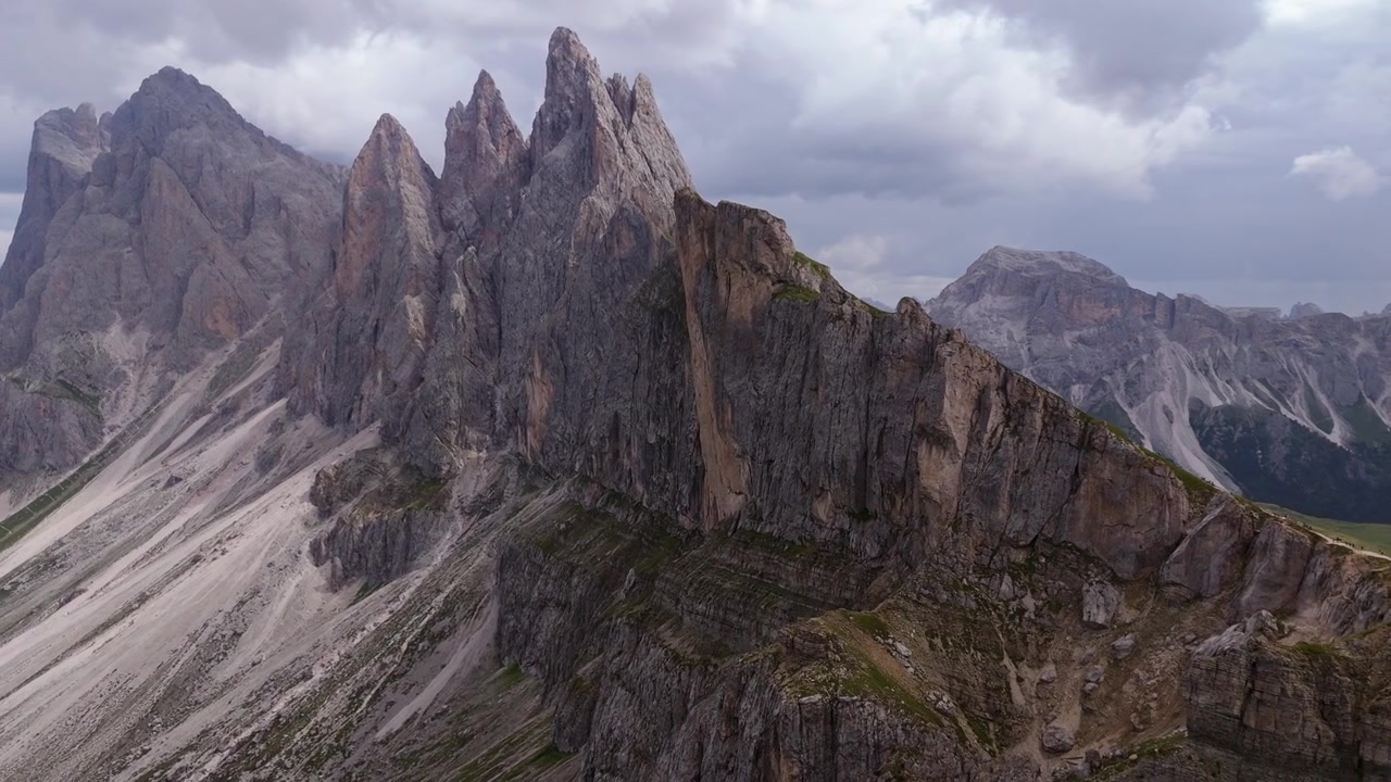 Low left orbit aerial highlighting the towering limestone cliffs and dramatic alpine landscape of Seceda in the Dolomites.
