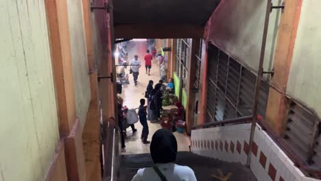 A woman wearing a hijab is going down the stairs after shopping at a traditional market.