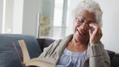 African-american-senior-woman-reading-a-book-while-sitting-on-the-couch-at-home
