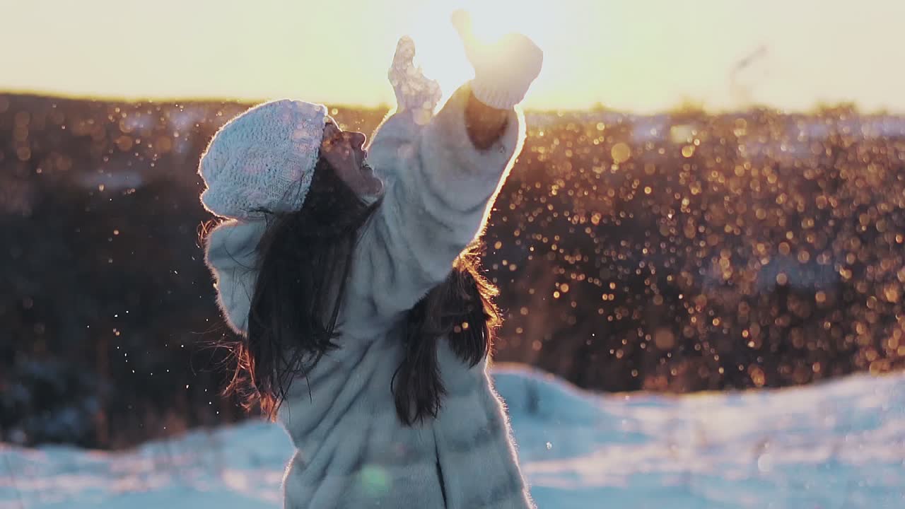 una joven muy sonriente arroja nieve iluminada por el sol de la tarde