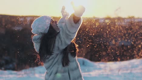 young pretty smiling woman throws snow lit by evening sun