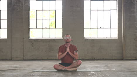 man in an industrial warehouse practicing yoga meditating on a mat.