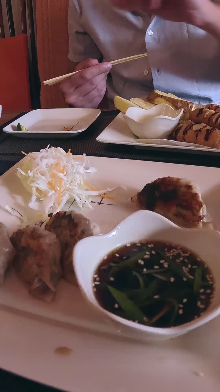 Person using chopsticks to pick up and dip fried dumplings or gyoza in soy sauce before eating it