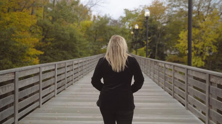 Blonde hair Caucasian woman walking on wooden footbridge exploring alone, follow shot from behind in 4k