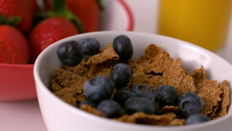 Blueberries-pouring-into-cereal-bowl-at-breakfast-table