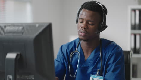 a black man sits at a computer in a doctor's uniform and writes a patient's card while taking calls with headphones. ambulance hotline receive calls and distribute ambulances