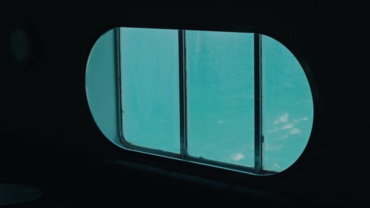 Rounded ship window glowing turquoise with the sea outside seen from a dark interior