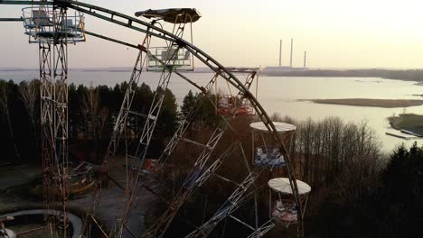 old abandoned ferris wheel carousel in front of power plant chimneys