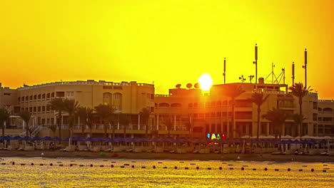 Zeitraffer-Der-Goldenen-Stunde:-Strand-Von-Hurghada-Mit-Palmen,-Gebäuden-Und-Majestätischer-Bergsilhouette-Bei-Sonnenuntergang
