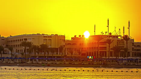 Time-lapse-De-La-Hora-Dorada:-Playa-De-Hurghada-Con-Palmeras,-Edificios-Y-Majestuosa-Silueta-De-Montaña-Al-Atardecer