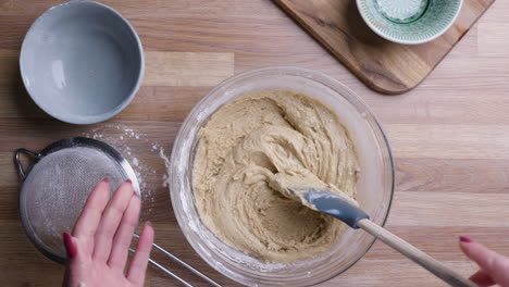 female hands mixing cake dough i glass bowl on wooden surface