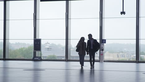 business couple at railway station wearing ppe face masks holding hands walking across concourse