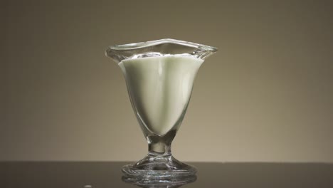 cerca de verter leche o yogur en el vidrio transparente aislado en fondo de pared beige. imágenes de stock. concepto de calcio y desayuno saludable.