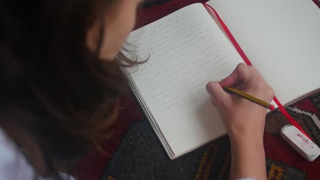 Brunette-woman-writing-on-her-diary-in-slow-motion-with-a-pencil-while-laying-on-the-carpet