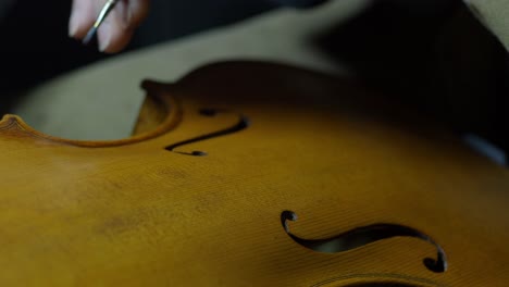 hands of a luthier precisely darkening violin edges, simulating natural wear and aging on the handcrafted instrument on edges and purfling, with finger and paintbrush traditional tecqnique