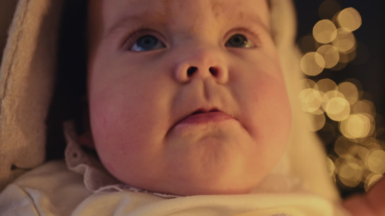 Close up of a baby's face with blue eyes and smooth, rosy skin with festive golden bokeh lights in the background